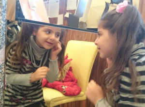 Petite fille devant un miroir, heureuse de pouvoir porter des boucles d'oreilles.